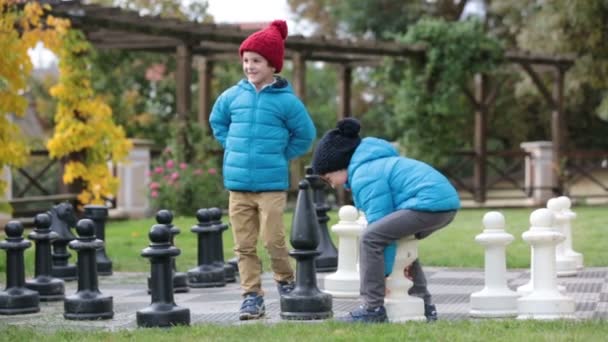 Due bambini, fratelli maschi, che giocano a scacchi con enormi figure nel parco a terra, ora d'autunno. Infanzia concetto di felicità, i bambini che giocano nel parco autunno tempo — Video Stock