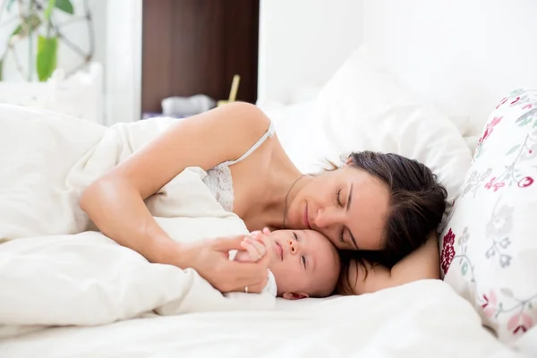 Jovem mãe dormindo com seu bebê, segurando-o em seus braços e — Fotografia de Stock