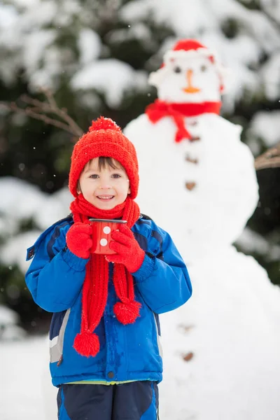 Gelukkig mooi kind gebouw sneeuwpop in tuin — Stockfoto