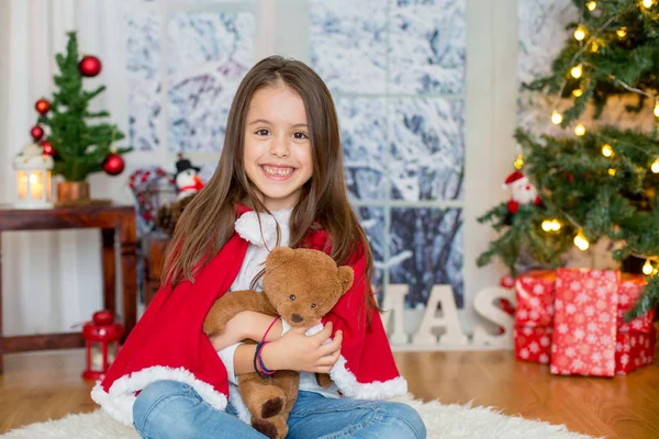 Šťastné dítě s hračkou sedí v přední části vánoční stromeček — Stock fotografie