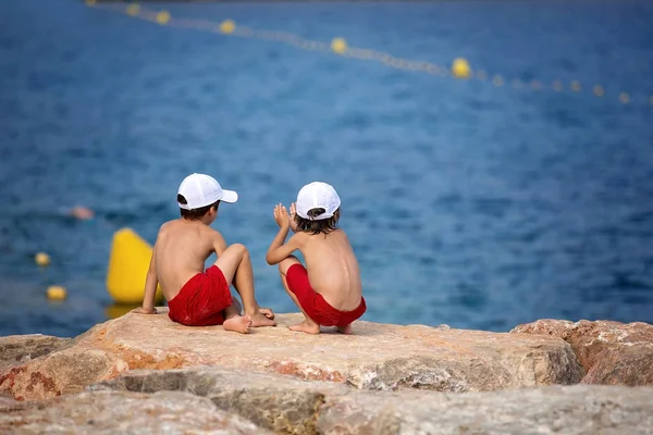 Dos chicos en la playa, divirtiéndose en un muelle de rocas — Foto de Stock