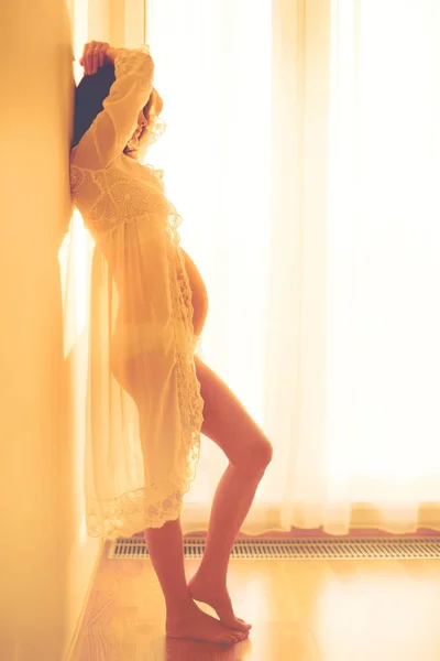 Beautiful young mom to be, leaning on a wall, watching out the e — Stock Photo, Image