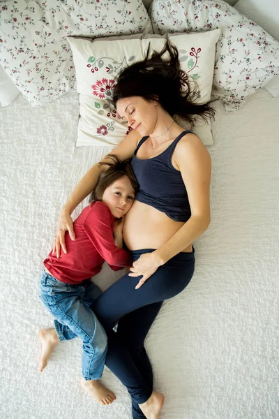 Piękna młoda matka w ciąży i jej dziecko, chłopiec, leżą w łóżku — Zdjęcie stockowe