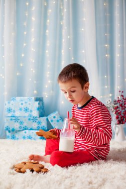 Sevimli küçük mutlu çocuk, çerezleri yiyip içmeyi bekliyor süt,