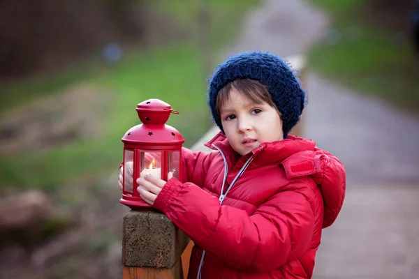 Dulce niño, sosteniendo linterna roja en el parque en un invierno soleado d — Foto de Stock