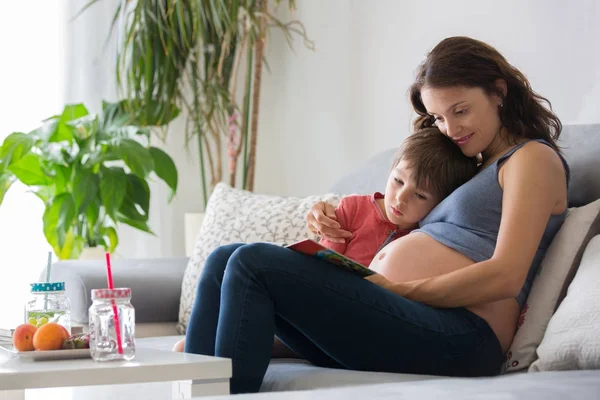 Unga gravid kvinna, läsa en bok hemma till hennes pojke — Stockfoto