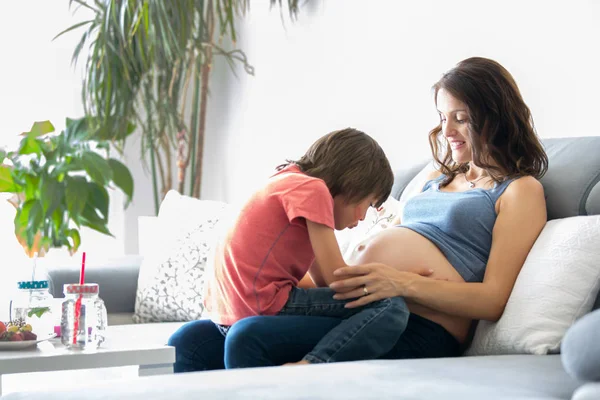 Jonge zwangere vrouw, het lezen van een boek thuis met haar jongen — Stockfoto