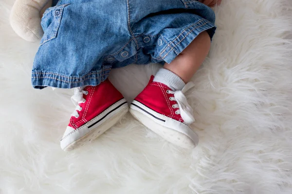 Zapatillas de deporte rojas de moda en los pequeños pies de los niños recién nacidos —  Fotos de Stock