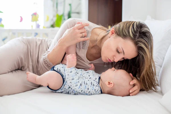 Молодая мать, лежа в постели со своим новорожденным мальчиком, играя — стоковое фото
