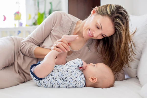 Joven madre, acostada en la cama con su bebé recién nacido, jugando — Foto de Stock