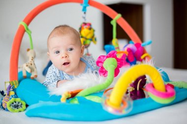 Cute baby boy on colorful gym, playing with hanging toys at home clipart