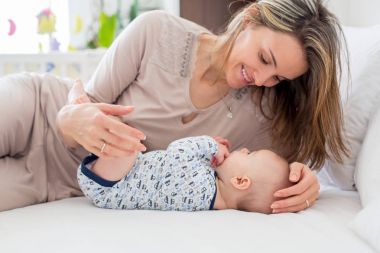 Genç anne ile oynarken onun yeni doğan bebek çocuk, yatakta yalan, 