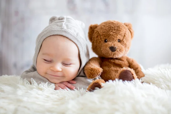 Sweet baby boy v medvěd celkově, spí v posteli s Medvídek — Stock fotografie