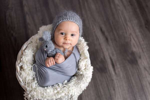 Sweet baby boy in basket, holding and hugging teddy bear, lookin
