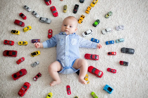 Очаровательный мальчик, лежащий на полу, игрушечные машины вокруг него — стоковое фото