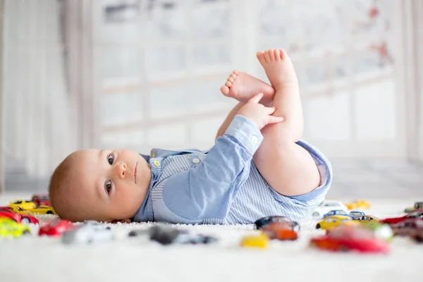 Adorável menino, deitado no chão, carros de brinquedo ao seu redor — Fotografia de Stock