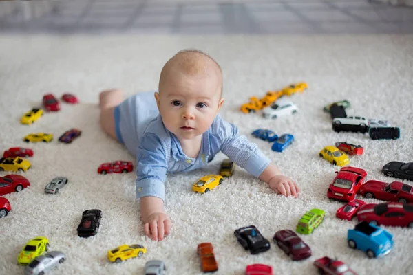 Очаровательный мальчик, лежащий на полу, игрушечные машины вокруг него — стоковое фото