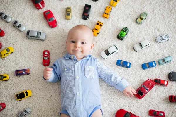 Чарівний хлопчик, лежить на підлозі, іграшкові автомобілі навколо нього — стокове фото