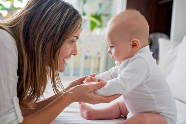 Joven madre acostada en la cama con su bebé recién nacido, jugando juntos — Foto de Stock