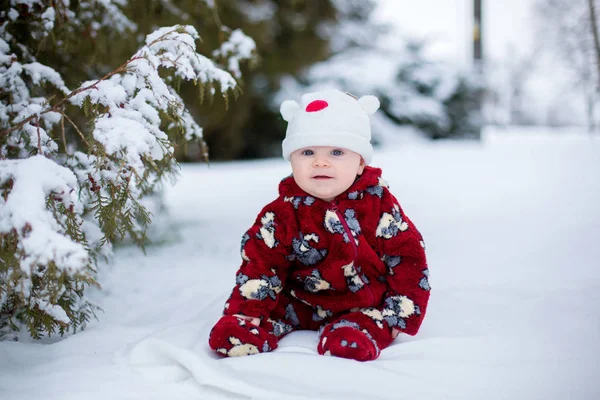 Kleiner süßer lächelnder Junge, der draußen im Schnee sitzt — Stockfoto