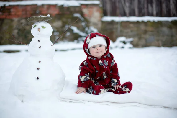 Kleiner süßer lächelnder Junge, der draußen im Schnee sitzt — Stockfoto