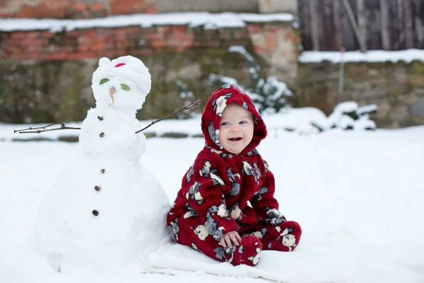 Liten söt leende pojke, sitter utomhus i snön — Stockfoto