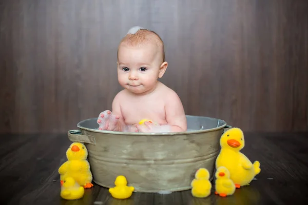 金属の洗面器に座りながらゴム製のアヒルと遊ぶかわいい赤ちゃん — ストック写真