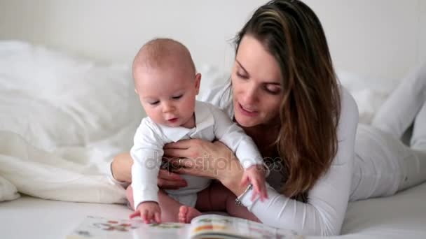 年轻的妈妈读了一本书给她的孩子 妈妈在家里看书给儿子在床上 — 图库视频影像
