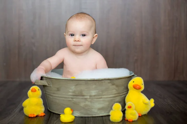 金属の洗面器に座りながらゴム製のアヒルと遊ぶかわいい赤ちゃん — ストック写真