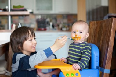 Sevimli okul öncesi çocuk, onun bebek kardeşi püresi sebze ile besleme
