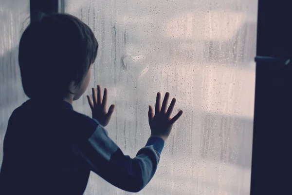 Маленький мальчик, оставляя отпечатки пальцев и рисуя сердца на окне — стоковое фото