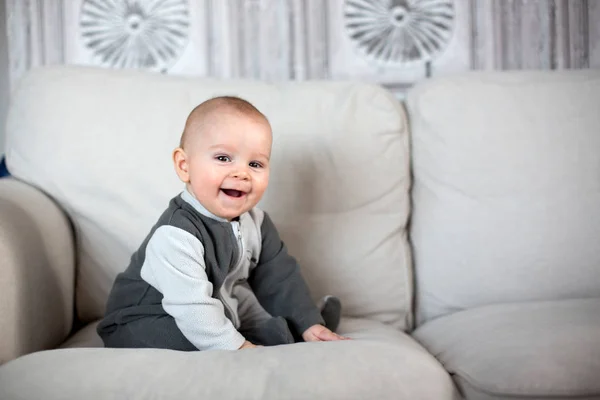 Little baby boy, sitting on a couch in a sunny living room — Stock Photo, Image