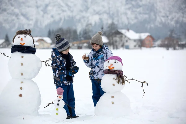 Семья с детьми, строит снеговика в парке в маленьком виле — стоковое фото