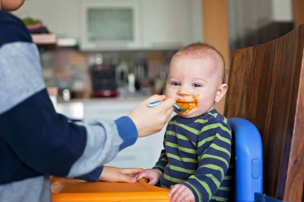 Lindo niño preescolar, alimentando a su hermano pequeño con puré de vegetales —  Fotos de Stock