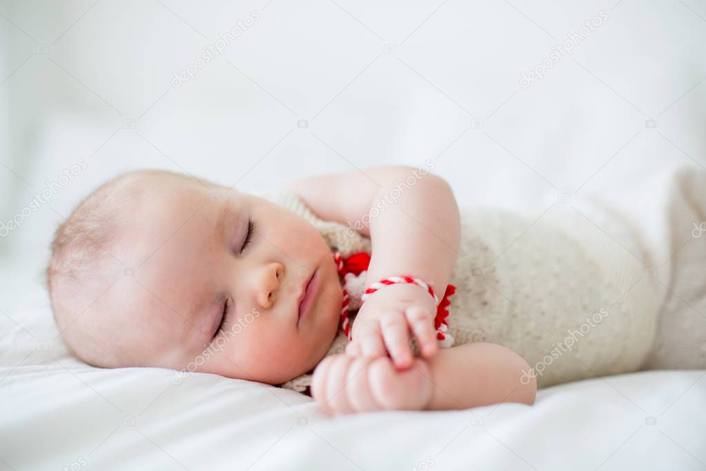 Cute baby toddler boy, sleeping with white and red bracelet. Martenitsa, white and red strains of yarn, Bulgarian folklore tradition, welcoming spring in March, adornment symbol, wish for good health