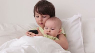 Küçük okul öncesi çocuk akıllı telefonda oynamak onun bebek kardeşi ile yatakta döşeme