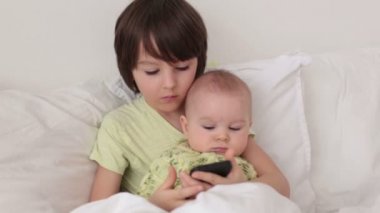 Küçük okul öncesi çocuk akıllı telefonda oynamak onun bebek kardeşi ile yatakta döşeme