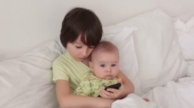Küçük okul öncesi çocuk akıllı telefonda oynamak onun bebek kardeşi ile yatakta döşeme
