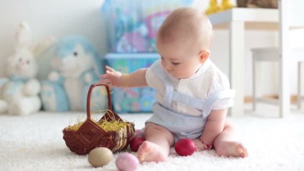 Aranyos kis tipegő gyermek, baba fiú, a napfényes nappali játszik a csokoládé húsvéti nyuszi és színes húsvéti tojás