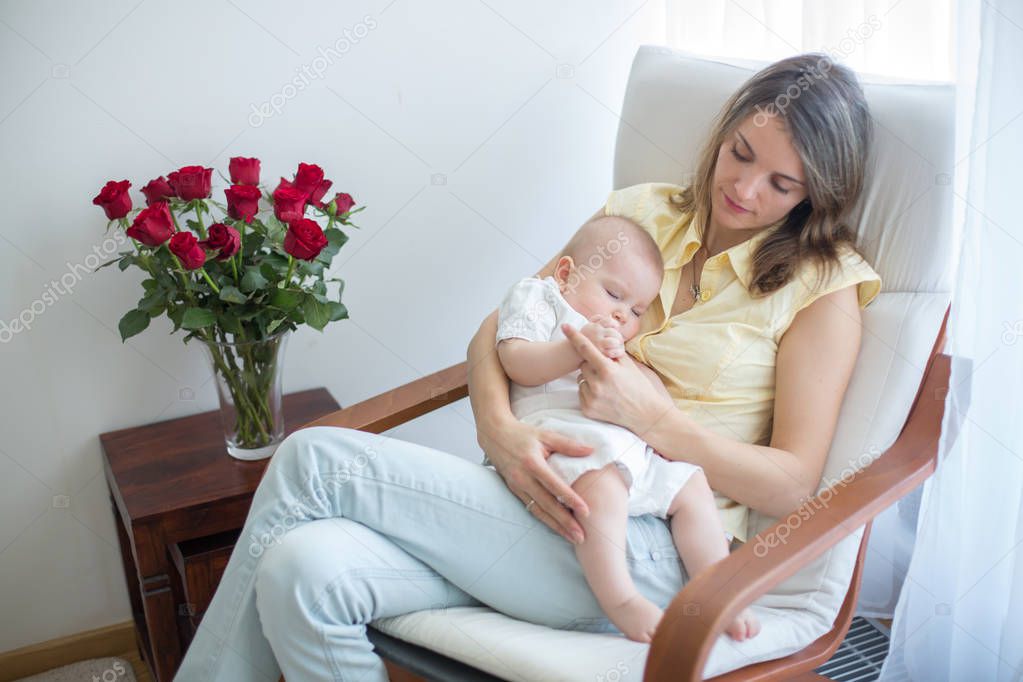 Young mother holding her baby, rocking him to sleep, sitting in 