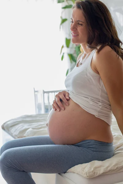 Happy young beautiful pregnant woman, sitting on bed in bedroom — Stock Photo, Image