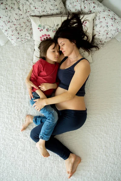 Schöne schwangere junge Mutter und ihr Kind, Junge, liegen im Bett — Stockfoto