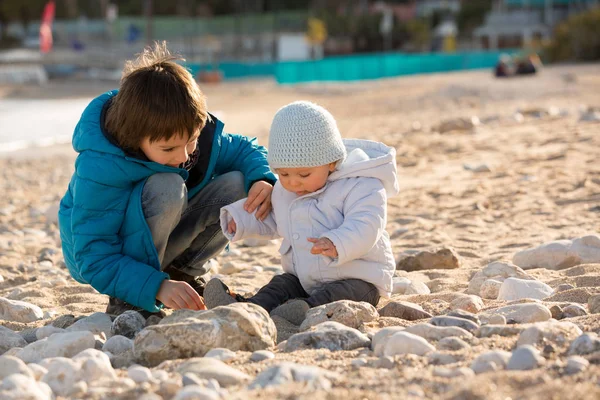 Lindos niños, hermanos, jugando en la playa con piedras de arena — Foto de Stock