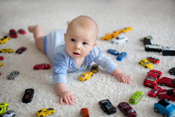Förtjusande baby pojke, liggande på golvet, leksaksbilar omkring honom — Stockfoto