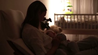 Genç güzel annem, emzirme gece, onun yeni doğan bebek çocuk loş ışık. Anne emzirme bebek.