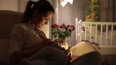 Genç güzel annem, emzirme gece, onun yeni doğan bebek çocuk loş ışık. Anne emzirme bebek.