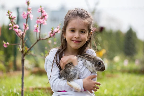 Маленькая девочка играет с белым кроликом в парке в солнечное лето — стоковое фото