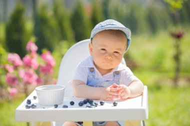 Mutlu yürümeye başlayan çocuk, bahçede güneşli sprin üzerinde yaban mersini yeme