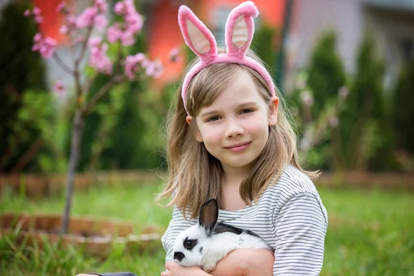 Маленькая девочка играет с белым кроликом в парке в солнечное лето — стоковое фото