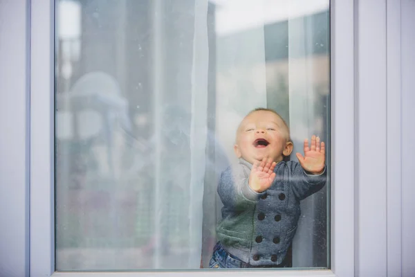 Ładny toddler chłopiec, pobyt w domu za szklanymi drzwiami, przeskakuje — Zdjęcie stockowe